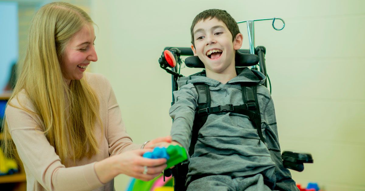 child in a wheelchair next to woman smiling while playing
